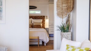 Une chambre à coucher avec un lit, des tables de chevet, une lampe, une plante et une vue sur l’extérieur.