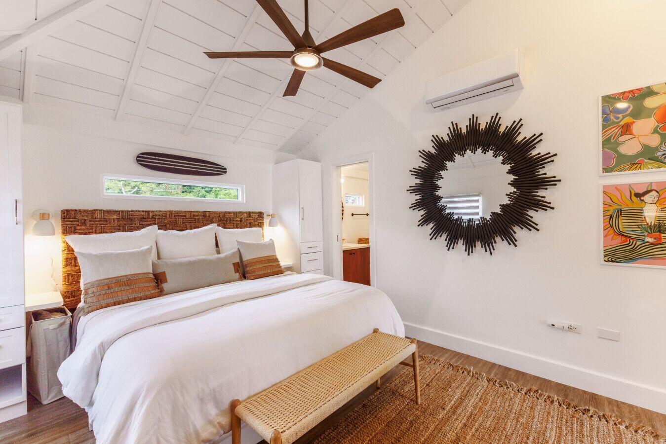 A bedroom with a large bed, a ceiling fan, a wall-mounted mirror, and artwork.