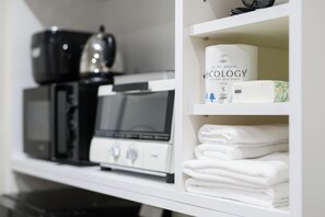 A kitchenette with a coffee maker, microwave, and kettle. There are white towels stacked on a shelf. - 9STAY Izutsu Kyoto Station (Kyoto)