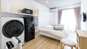 A compact hotel room with a bed, a desk, a washing machine, and a refrigerator.