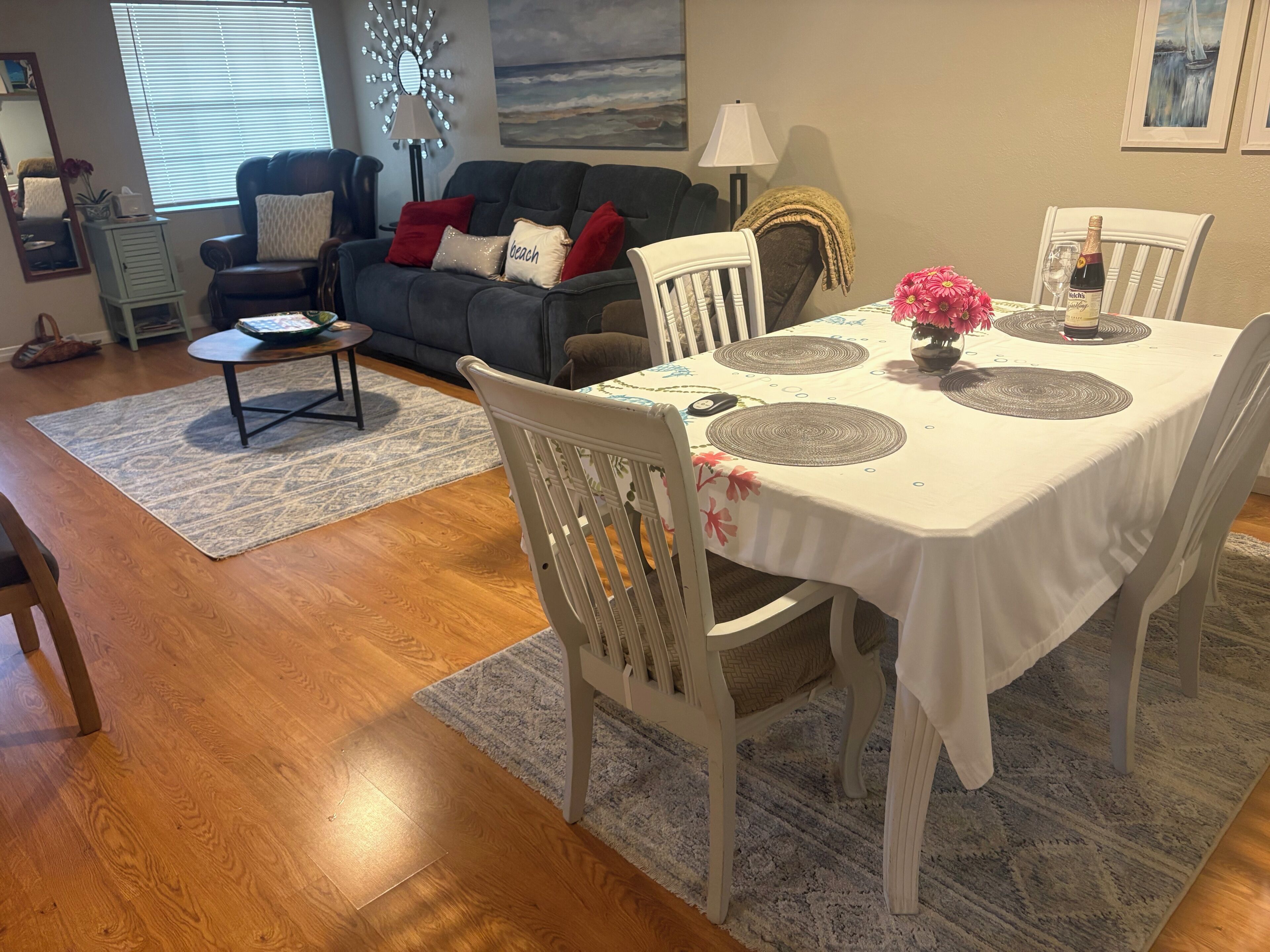 A dining area with a white table set for four, surrounded by white chairs, with a tablecloth and placemats.