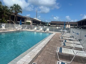 A swimming pool with lounge chairs and a white fence.