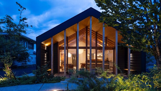 A modern house with a large open porch, wooden beams, and a well-lit interior.