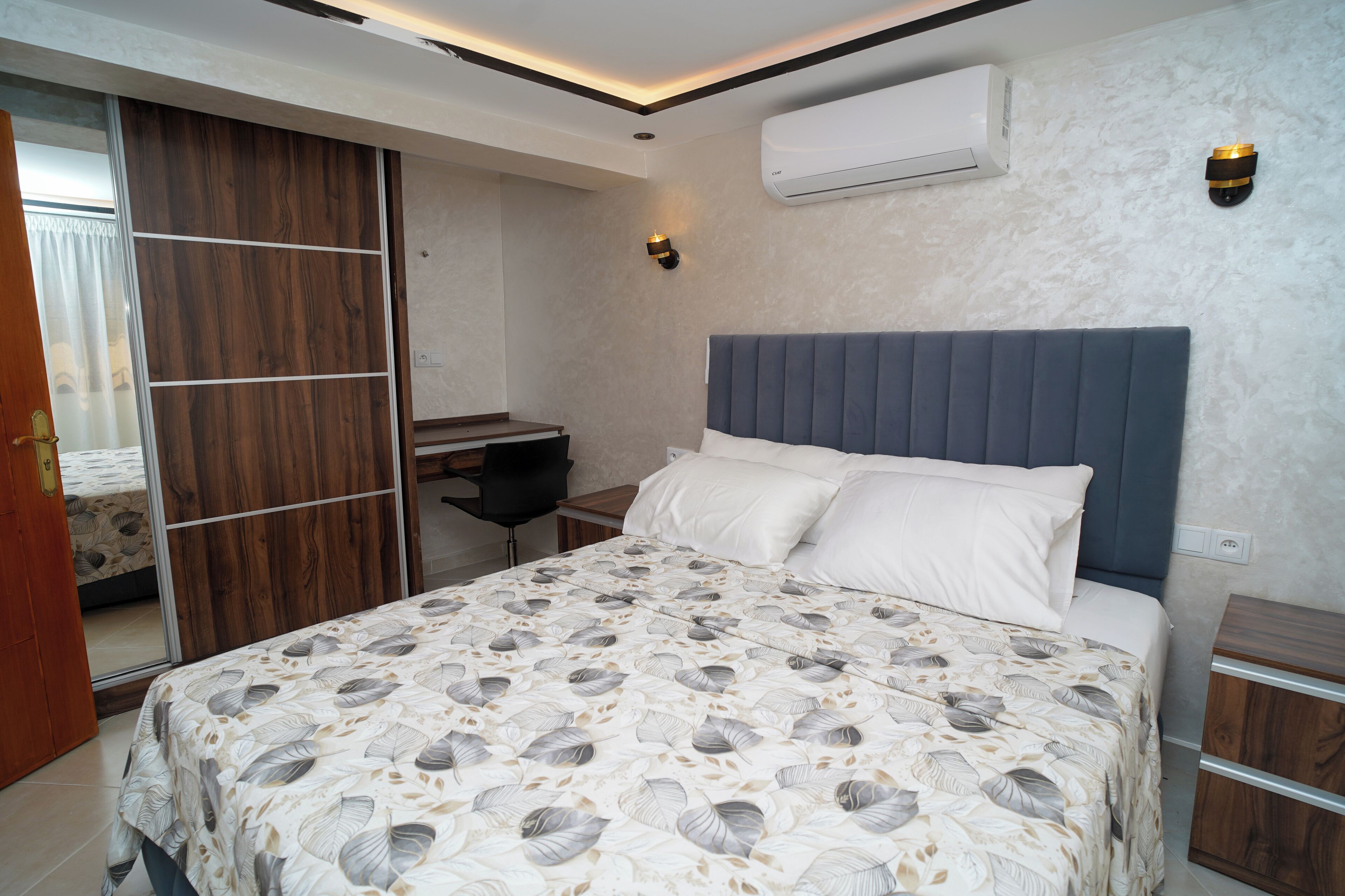 A bedroom with a bed, a desk, and an air conditioning unit.