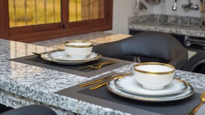 A dining area with a granite countertop, two white bowls with gold rims, and matching cutlery on a placemat.