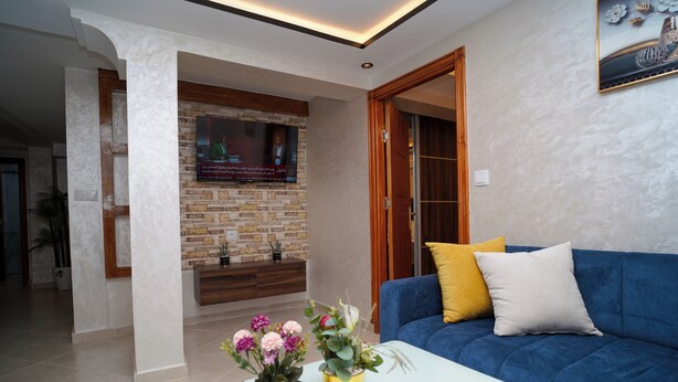 A modern living room with a blue sofa, two gold vases with flowers, a white coffee table, and a brick wall with a window.