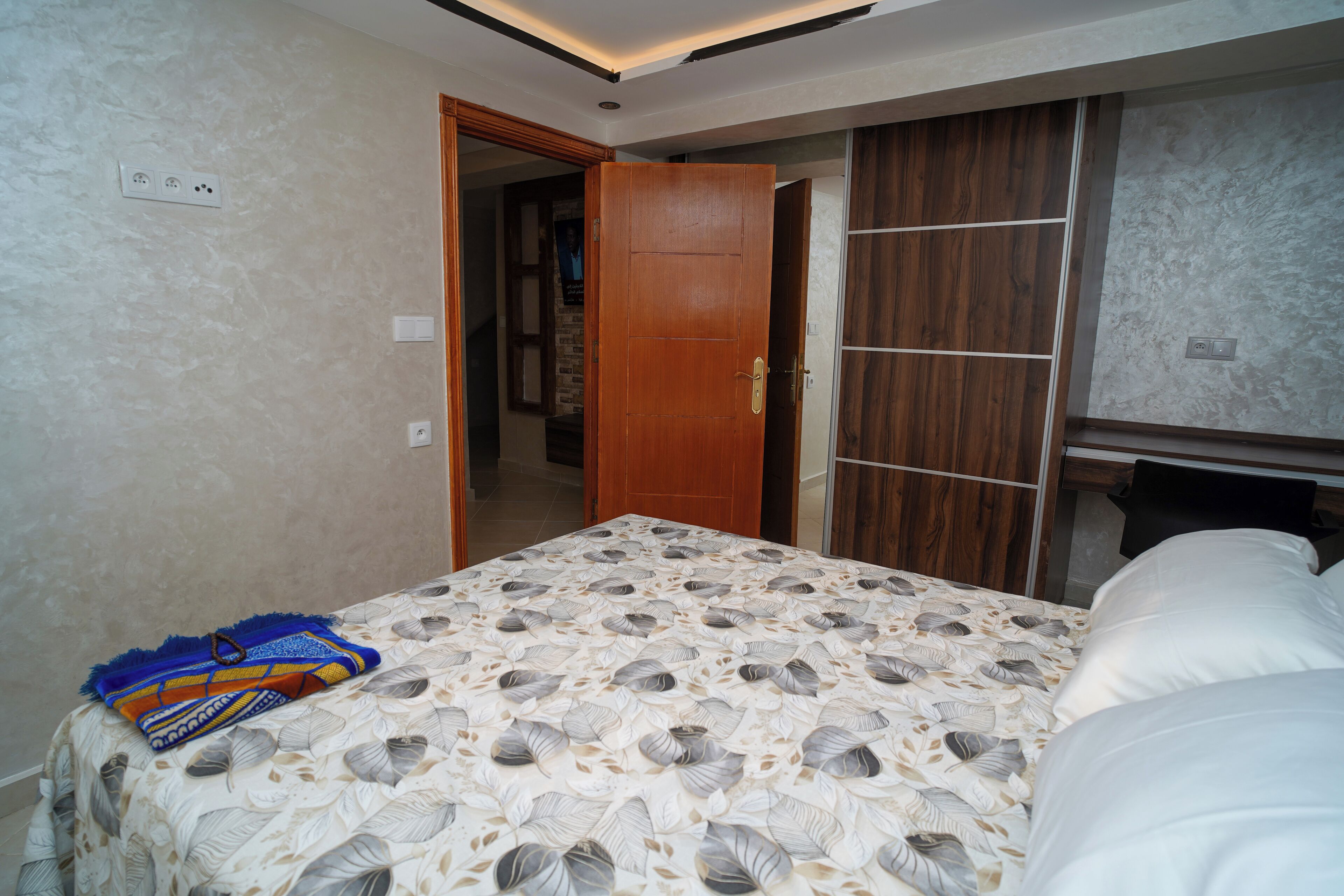 A bedroom with a bed, a wardrobe, and a door leading to another room.