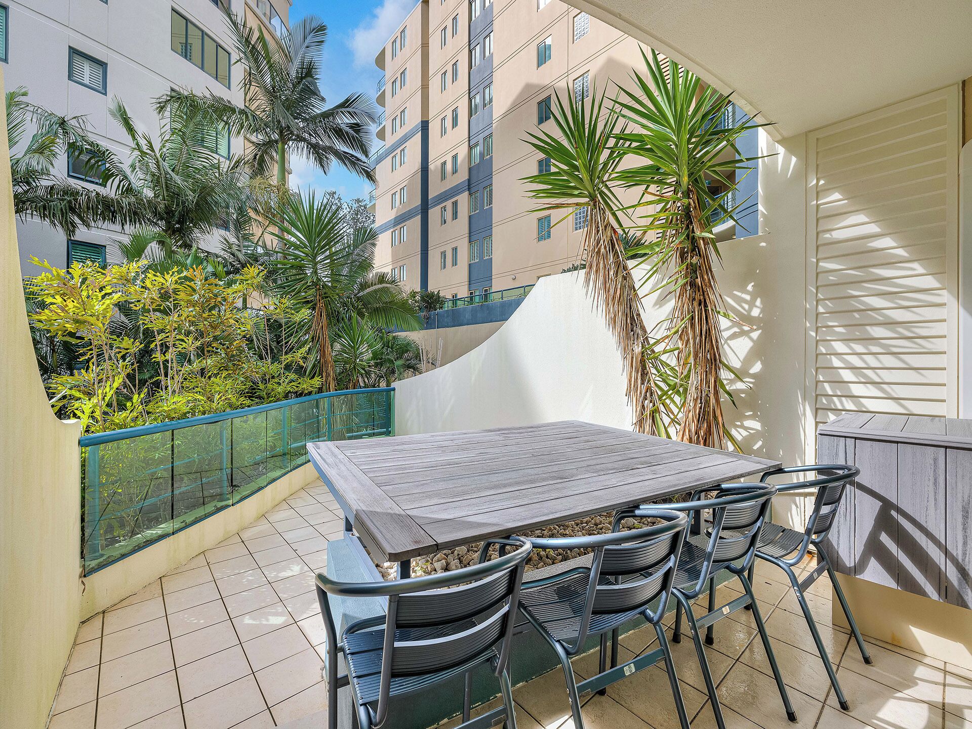 Un balcon avec une table et des chaises en bois, entouré de plantes et offrant une vue sur un immeuble.
