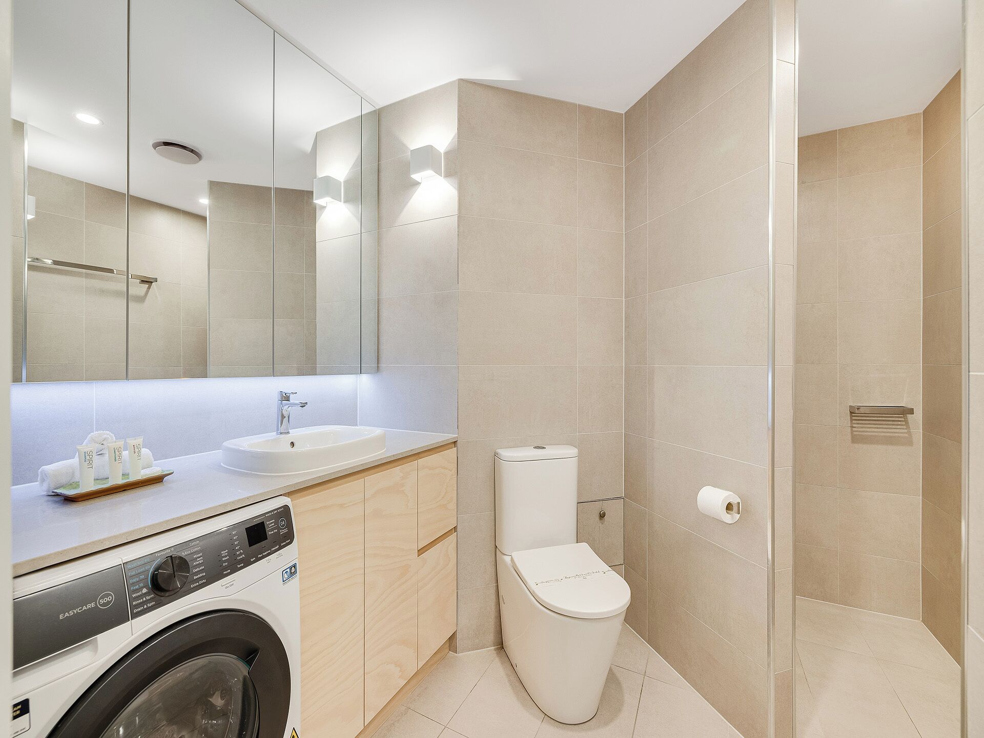 A modern bathroom with a washing machine, a toilet, and a shower area.