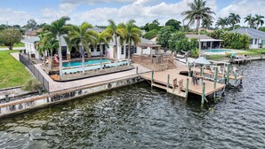 A waterfront property with a swimming pool, dock, and palm trees.