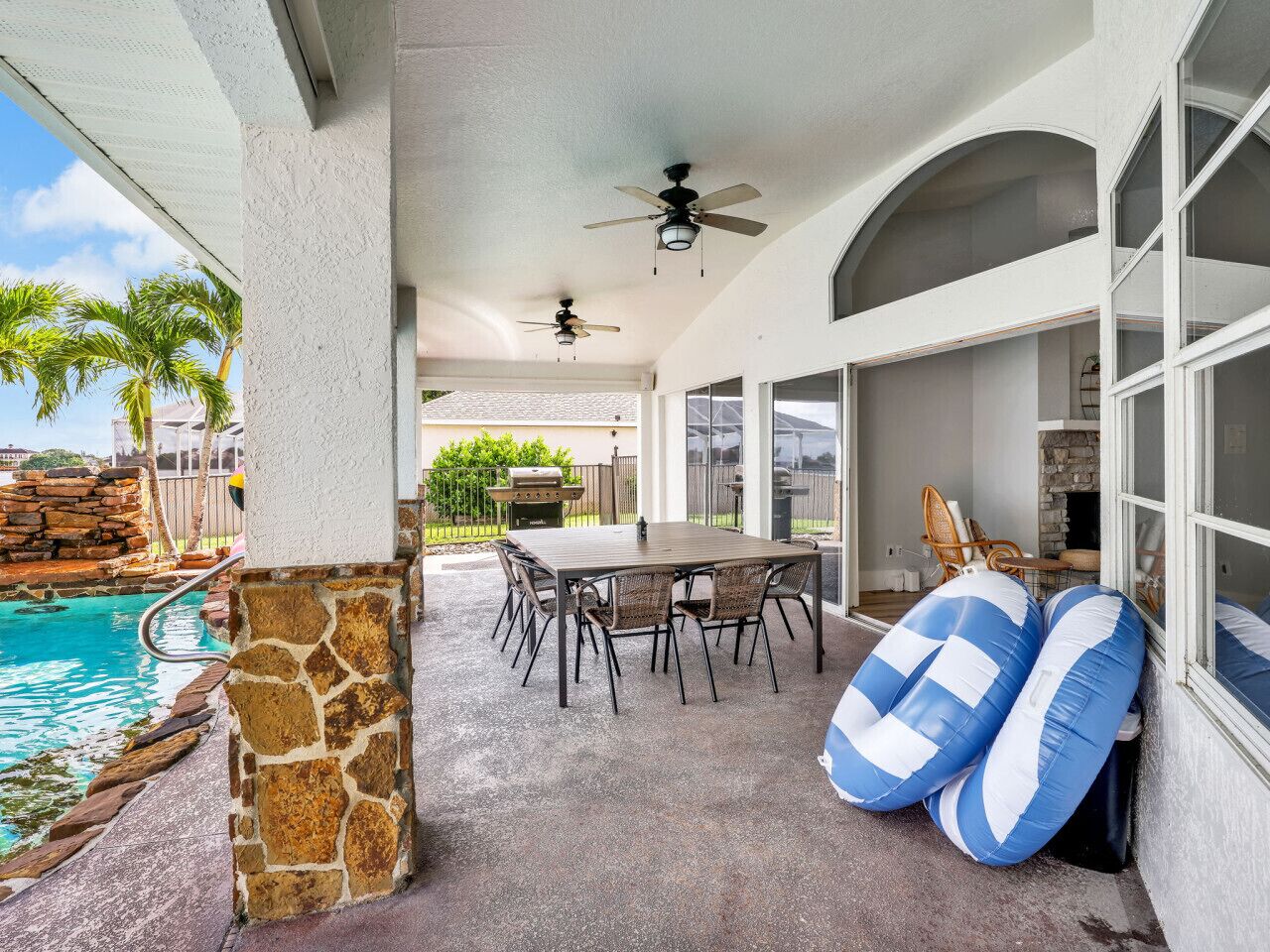 A covered patio with a pool, a table with chairs, and two inflatable rings.