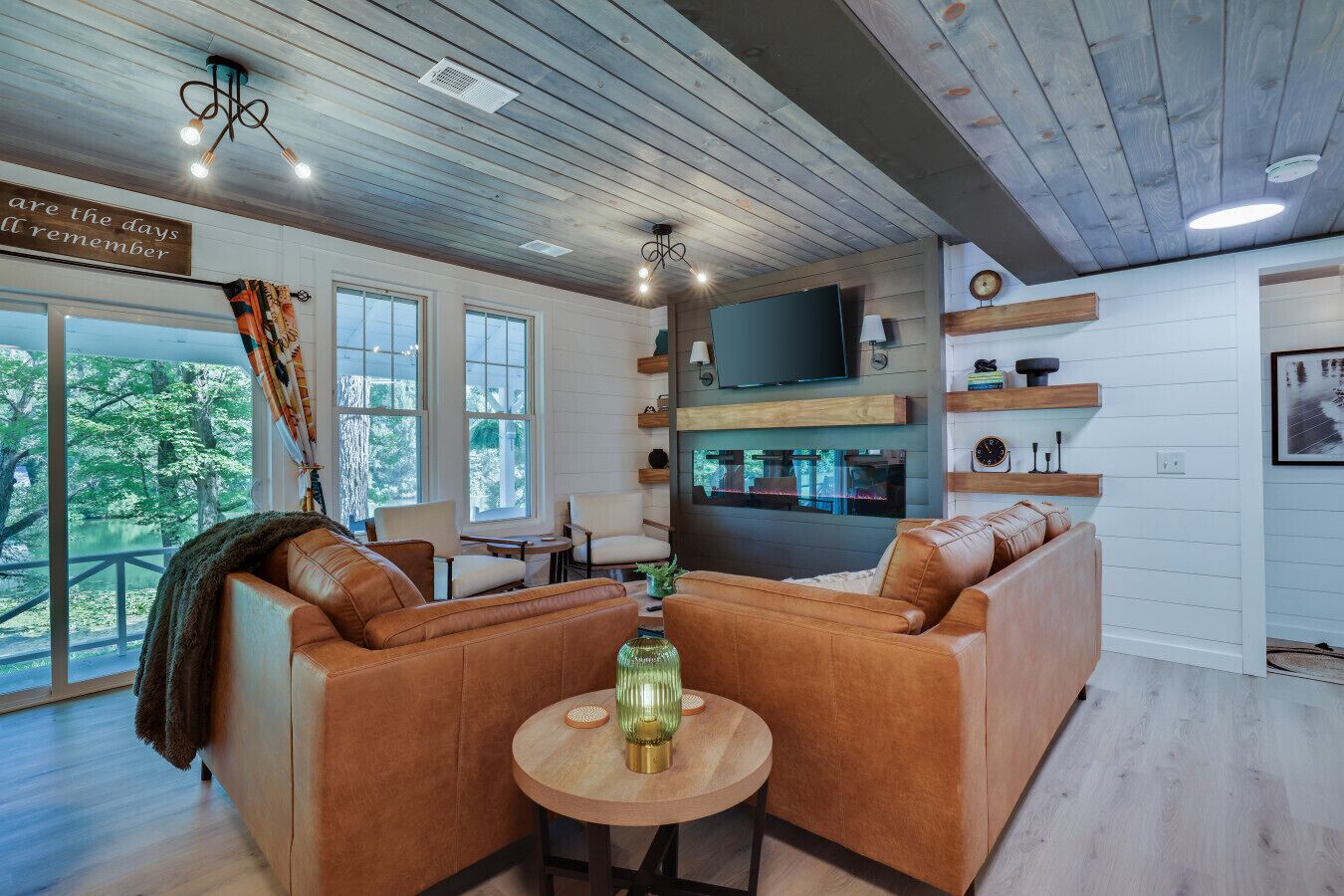 A cozy living room with a leather sofa, a round wooden table, and a TV mounted on the wall.