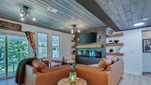 A cozy living room with a leather sofa, a round wooden table, and a TV mounted on the wall. - Heatherbell, A Lakeside Retreat (Saylorsburg)