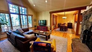 A cozy living room with a fireplace, a sofa, a coffee table, and a dining area with a chandelier. - Walk to Downtown Graeagle, Mill Pond & Pickleball (Graeagle)