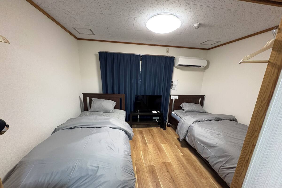 Habitación de hotel con dos camas, televisión, aire acondicionado y piso de madera.