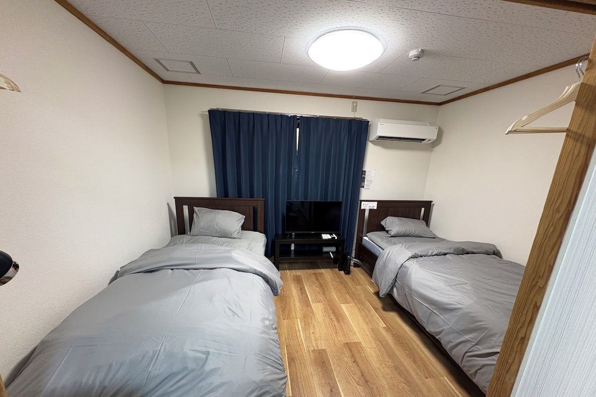 Une chambre d’hôtel avec deux lits, une télévision, un climatiseur et un plancher en bois.