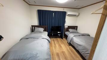 A hotel room with two beds, a TV, an air conditioner, and a wooden floor.