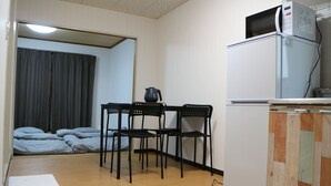 Ein gemütlicher Raum mit Küchenzeile, einem Bett mit grauer Bettwäsche und einem Essbereich mit Stühlen.