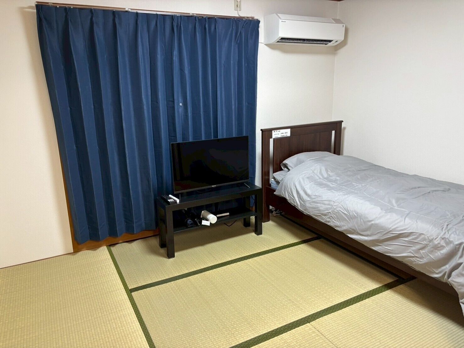 A room with a bed, a TV on a stand, an air conditioner, and a curtain.