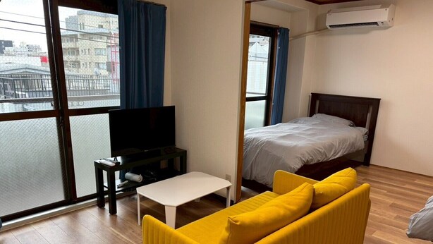 Ein Zimmer mit einem Bett, einem Sofa, einem Fernseher und einem Fenster mit Blick auf Gebäude.