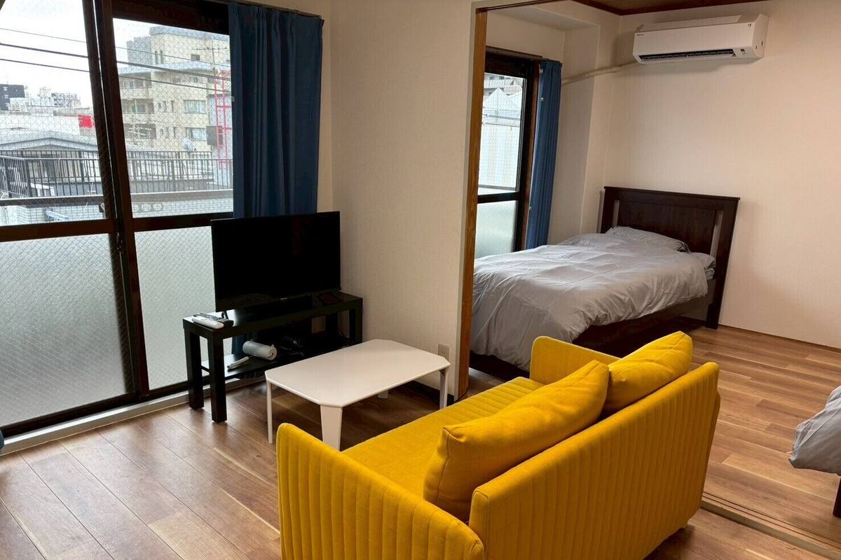 Una habitación con cama, sofá, televisor y ventana con vista a edificios.