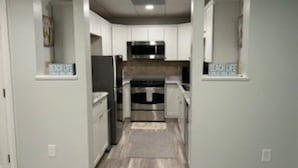 A narrow hallway leading to a kitchen with white cabinets, a microwave, and an oven. - Cozy Quiet Whole Apartment Haven for Rent (Grayson)