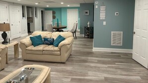 A living room with a beige sofa, a glass coffee table, and teal cushions. There is a dining area with a table and chairs in the background. - Cozy Quiet Whole Apartment Haven for Rent (Grayson)