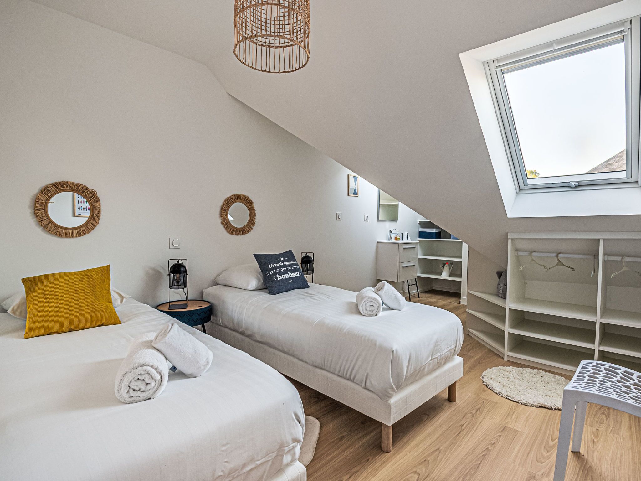 A modern bedroom with two beds, a skylight, a wardrobe, and a desk.