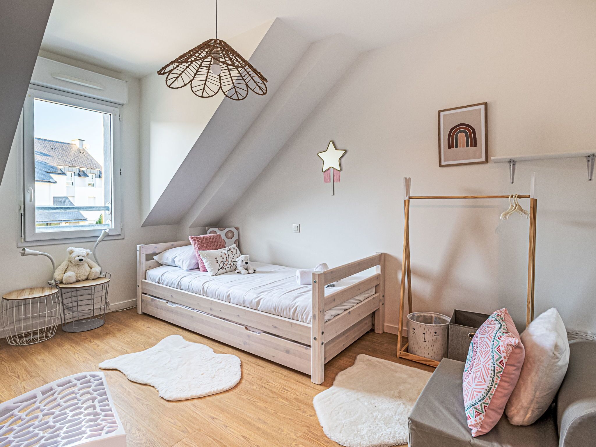A cozy bedroom with a loft bed, a hanging light fixture, a star decoration, and a view of buildings outside the window.