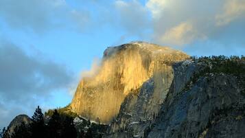 A mountain with a prominent peak, surrounded by trees and under a partly cloudy sky.