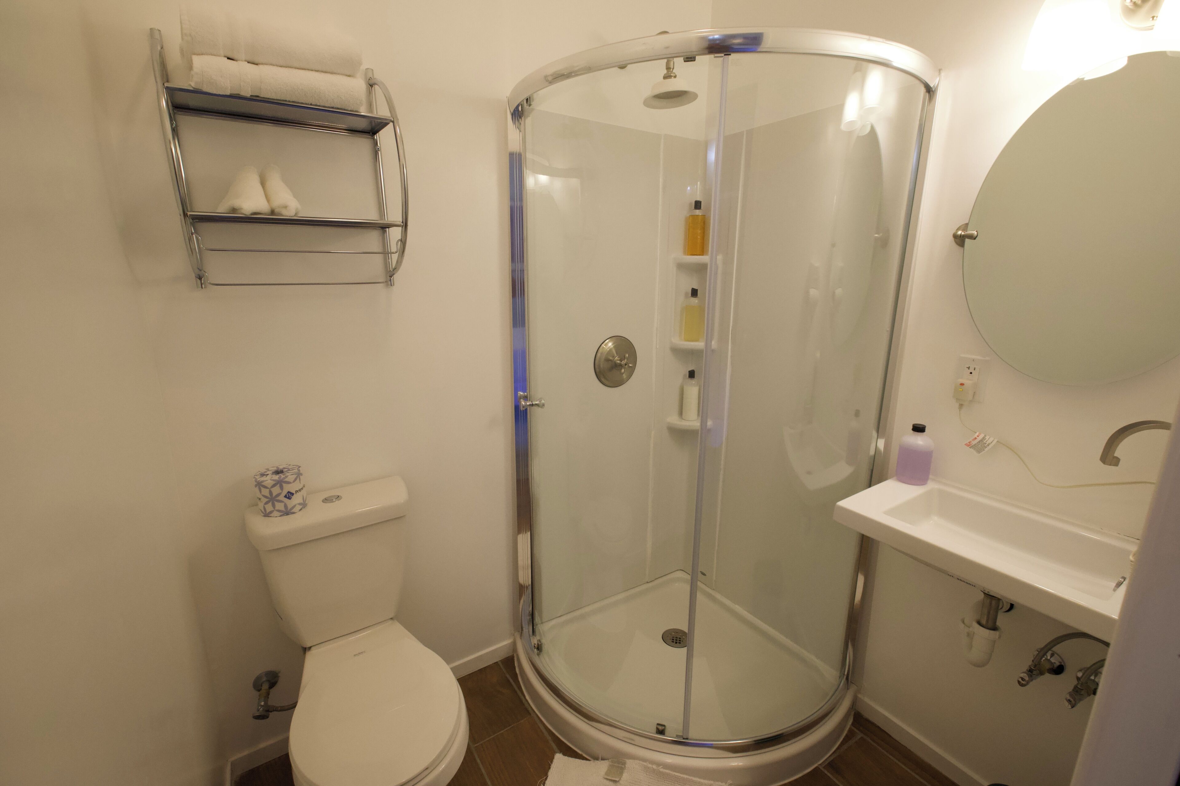 A bathroom with a glass-enclosed shower, a toilet, a sink, and a shelf with towels.