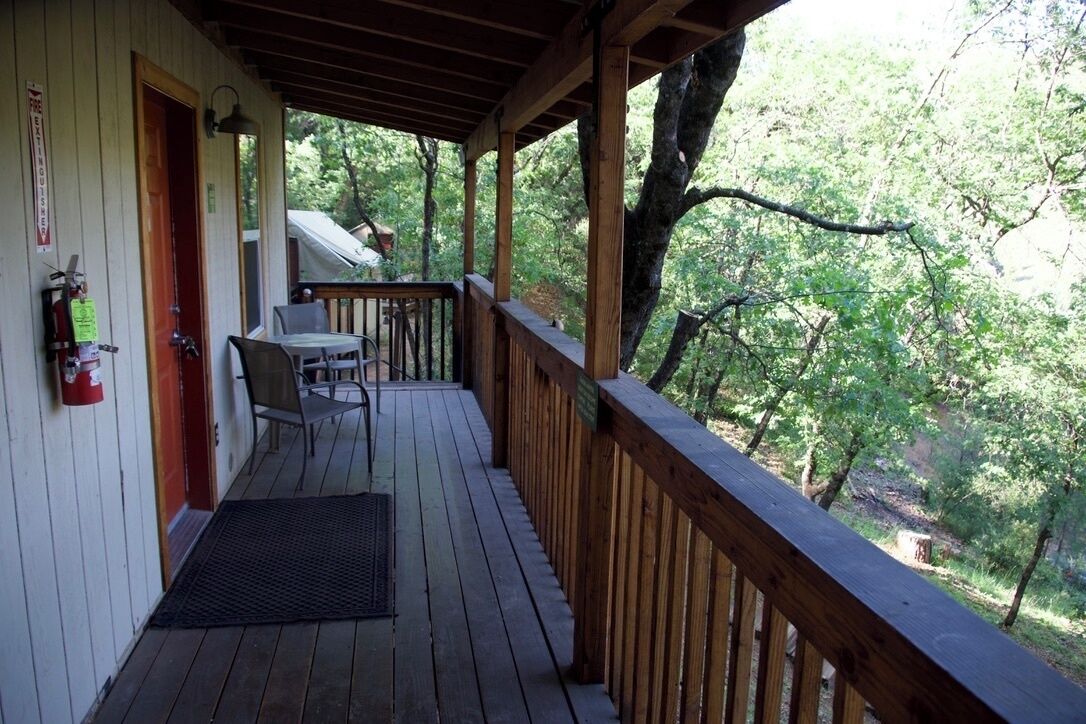 A wooden deck with a railing, a fire extinguisher, and a covered seating area.