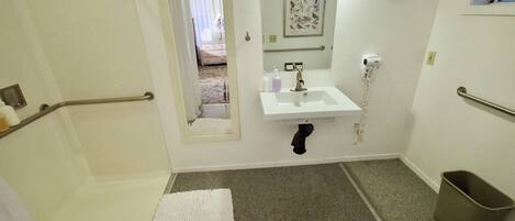 A bathroom with a white sink, a mirror, a shower, and a toilet.