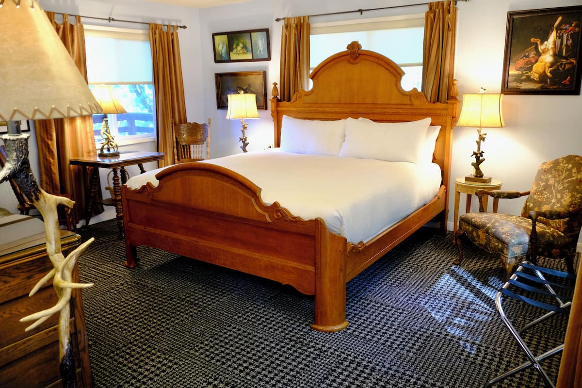 Ein stilvolles Hotelzimmer mit einem großen hölzernen Bett, einem Sessel, einem kleinen Tisch und einer Lampe.