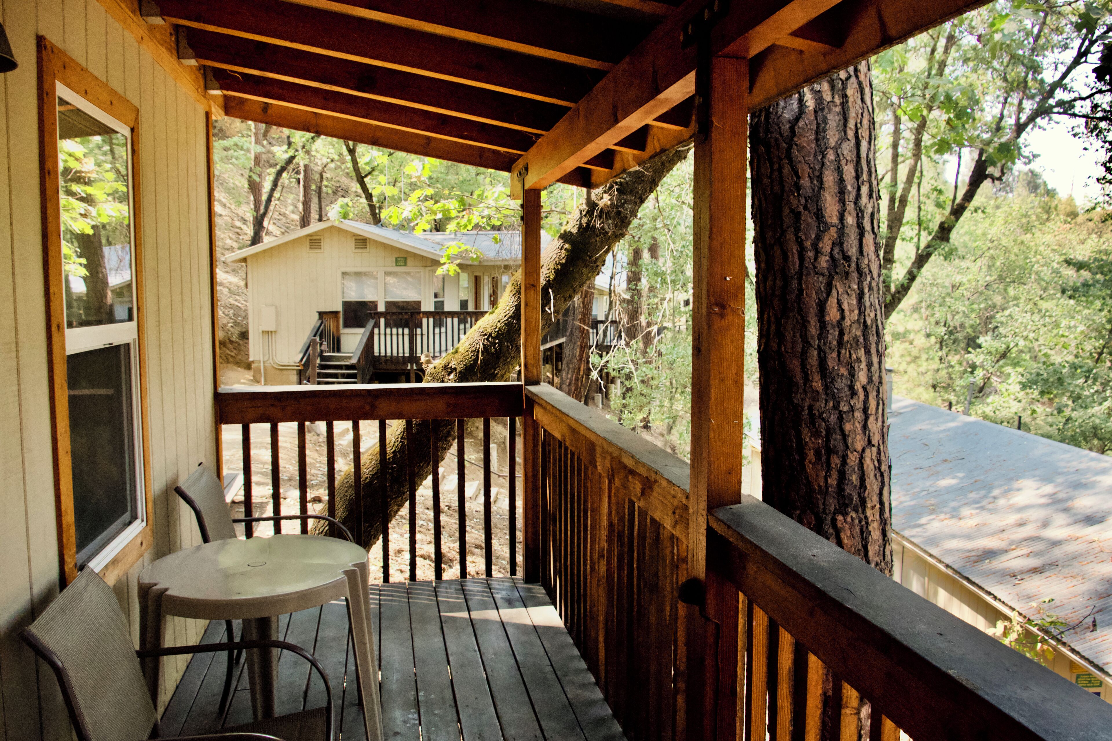 Une terrasse en bois avec une table et des chaises, d’où l’on a vue sur une maison et une route.