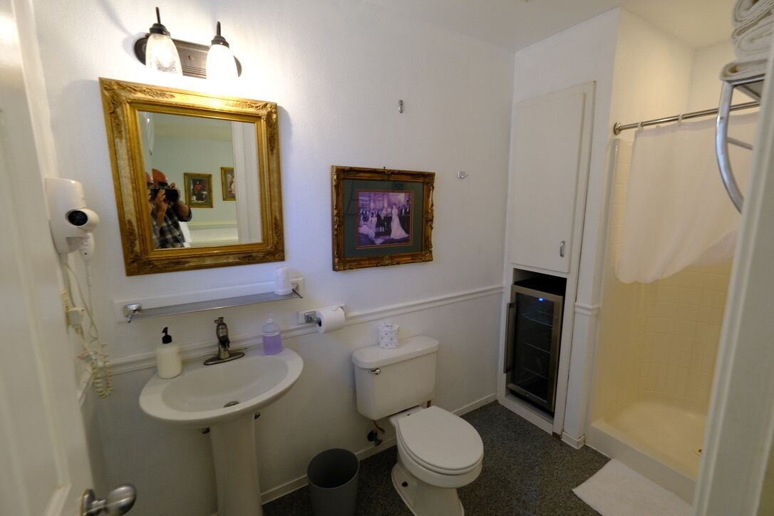 A bathroom with a white sink, toilet, and shower. There is a mirror with a gold frame and two wall-mounted lights.