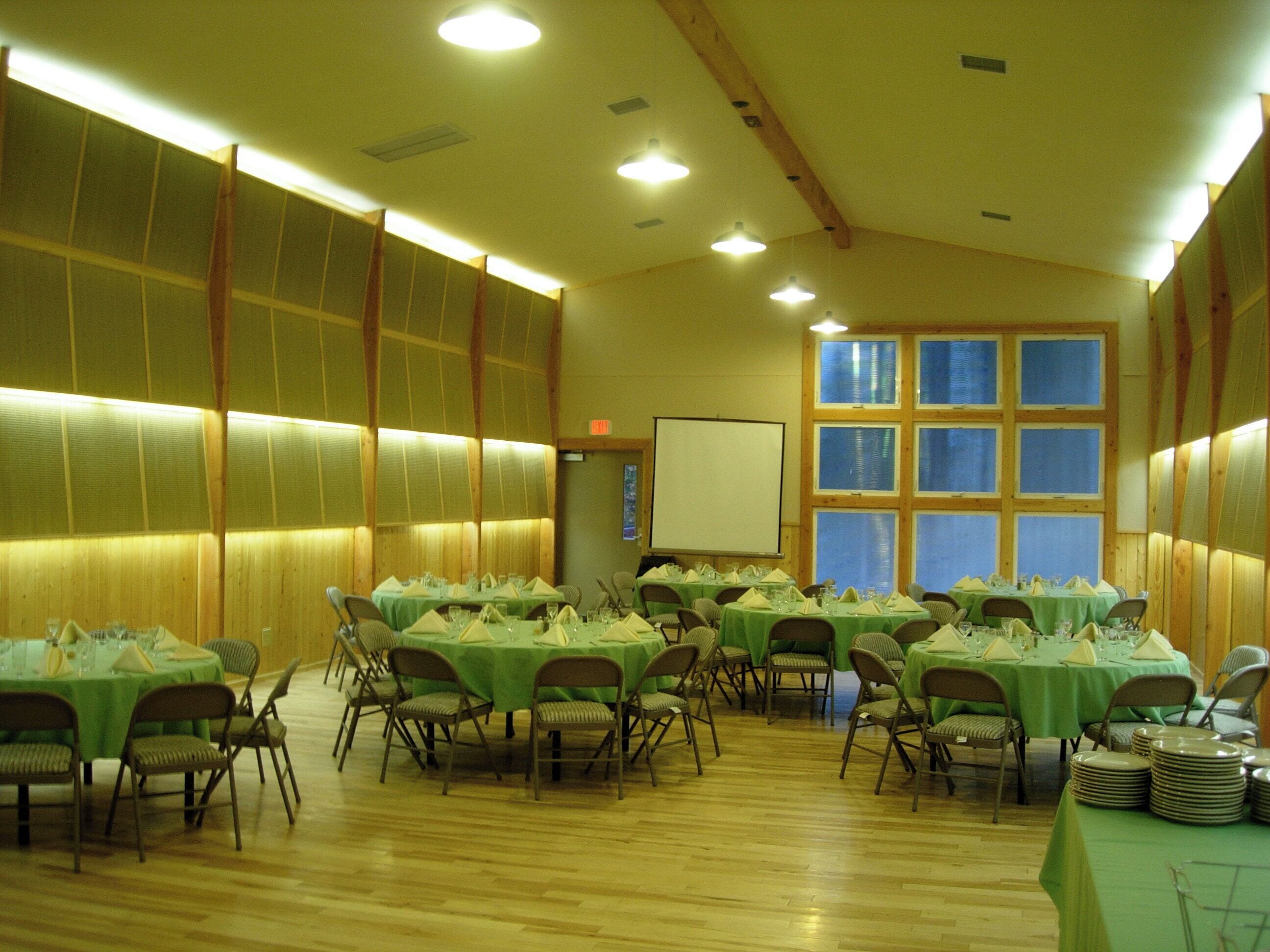 A conference room with multiple tables set for dining, equipped with chairs and a projector screen.