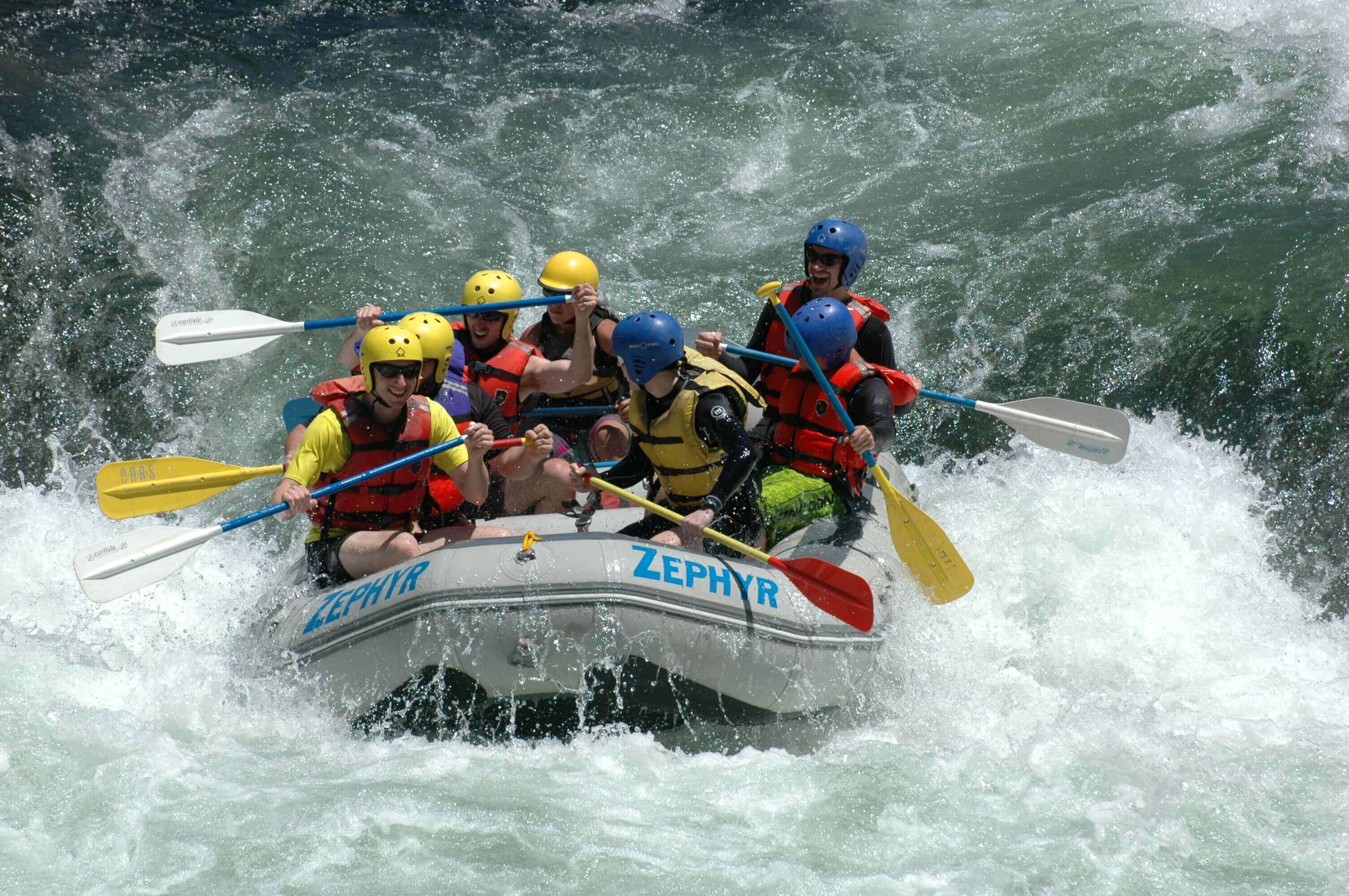 A group of people in a white inflatable raft with the brand name 'ZEPHYR' on it, paddling through rough waters.