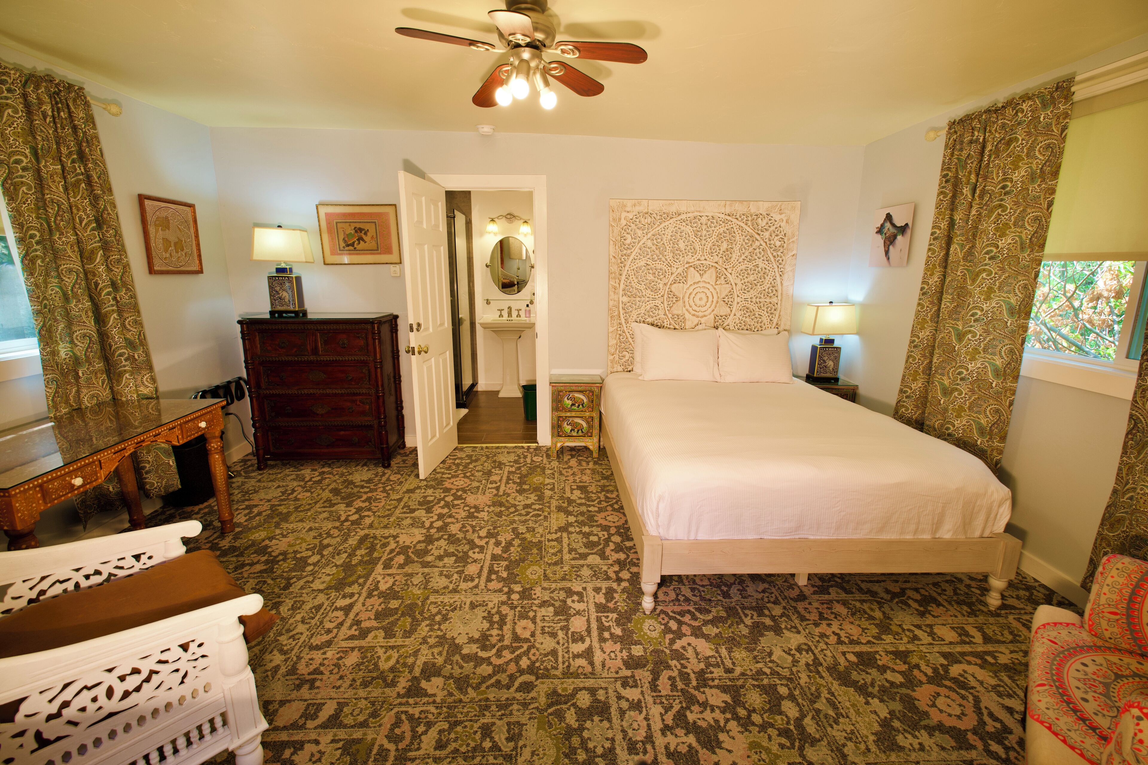 A bedroom with a bed, a desk, a dresser, a mirror, and a ceiling fan.