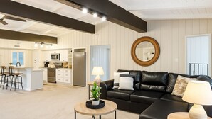 A modern living room with a black leather sofa, a round coffee table, and a dining area with a kitchen in the background. - Brookhollow Escape at Ransom Canyon (Ransom Canyon)