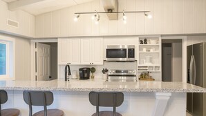 A modern kitchen with white cabinetry, a granite countertop, stainless steel appliances, and a bar area with stools. - Brookhollow Escape at Ransom Canyon (Ransom Canyon)