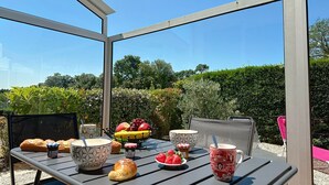 Un tavolo apparecchiato all'aperto, protetto da una struttura in vetro, con diversi cibi e vista sul giardino circostante.