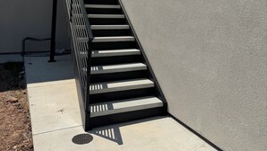 Eine Treppe führt zu einem Gebäude mit einer strukturierten Wand und einem Metallgeländer.