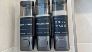 Drei Flaschen Duschgel, Conditioner und Shampoo auf einer gefliesten Wand.