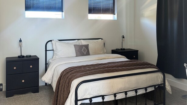 Ein Schlafzimmer mit einem Bett, zwei Nachttischen, einem Deckenventilator und zwei Fenstern mit Jalousien.