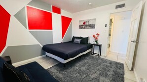 A modern bedroom with a bed, a small bedside table with a vase of flowers, and a geometric wall design. - Charming 3-bedroom house with an outdoor pool, WiFi, &AC in phenomenal Las Vegas (Las Vegas)