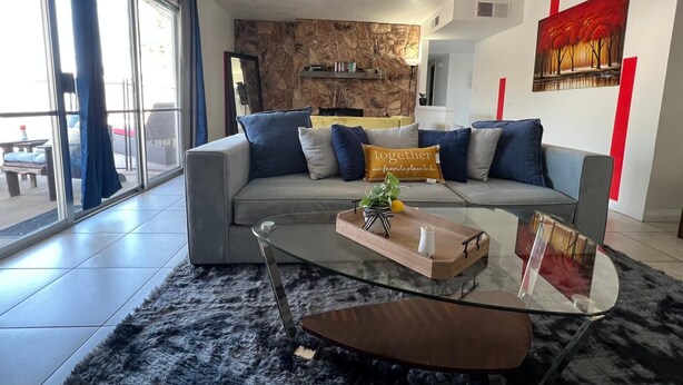 A modern living room with a grey sofa, blue cushions, a glass coffee table, and a stone wall. - Charming 3-bedroom house with an outdoor pool, WiFi, &AC in phenomenal Las Vegas (Las Vegas)