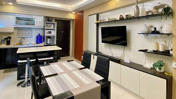 Een moderne keuken met inbouwapparatuur, een eethoek met een tafel en stoelen, en een flatscreen televisie aan de muur.