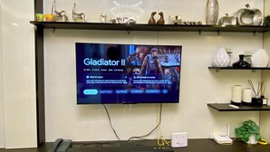 Een moderne receptie met een flatscreen-tv waarop 'Gladiator II' wordt vertoond, een telefoon en een kleine plant.