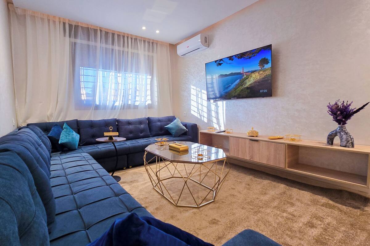A modern living room with a sectional sofa, a coffee table, and a TV mounted on the wall.